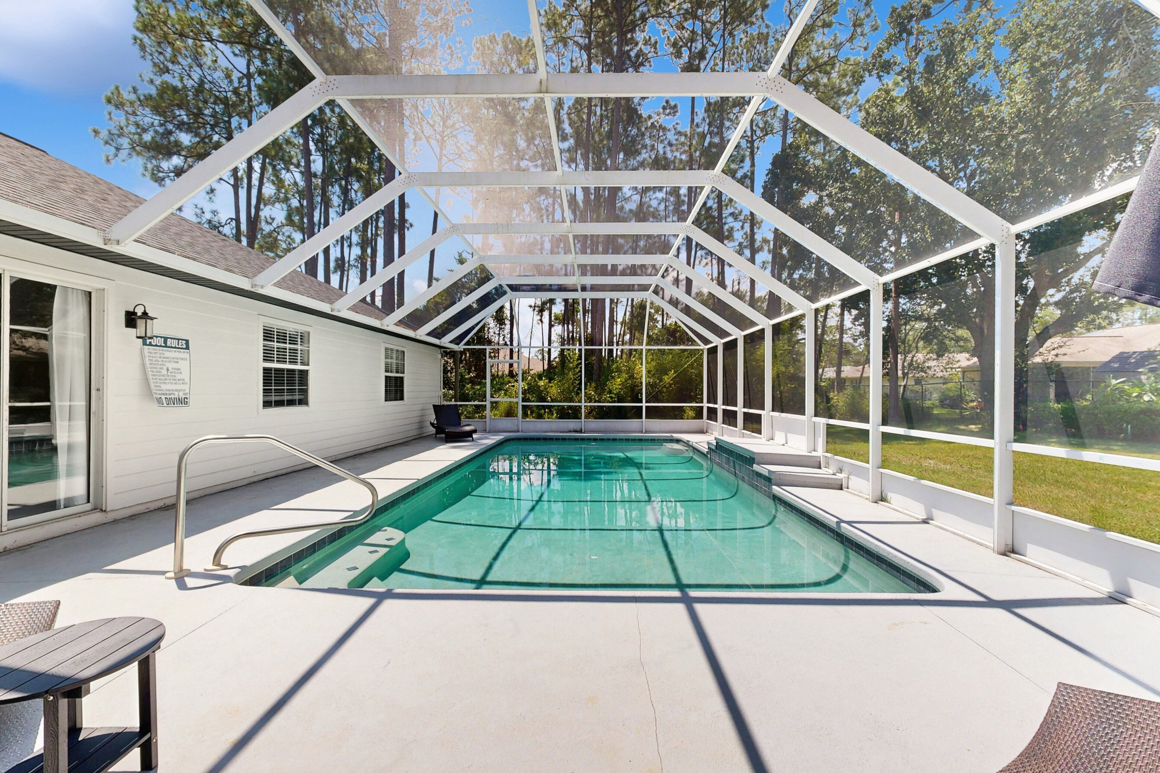 Una piscina exterior techada con estructura metálica, una silla de descanso y un letrero que indica que no está permitido bucear.
