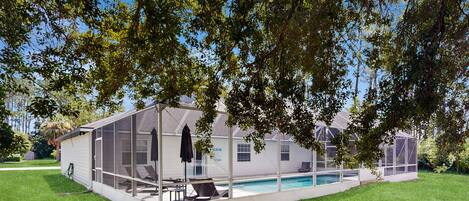 A modern house with a large glass-enclosed patio area, a swimming pool, and a well-maintained lawn.