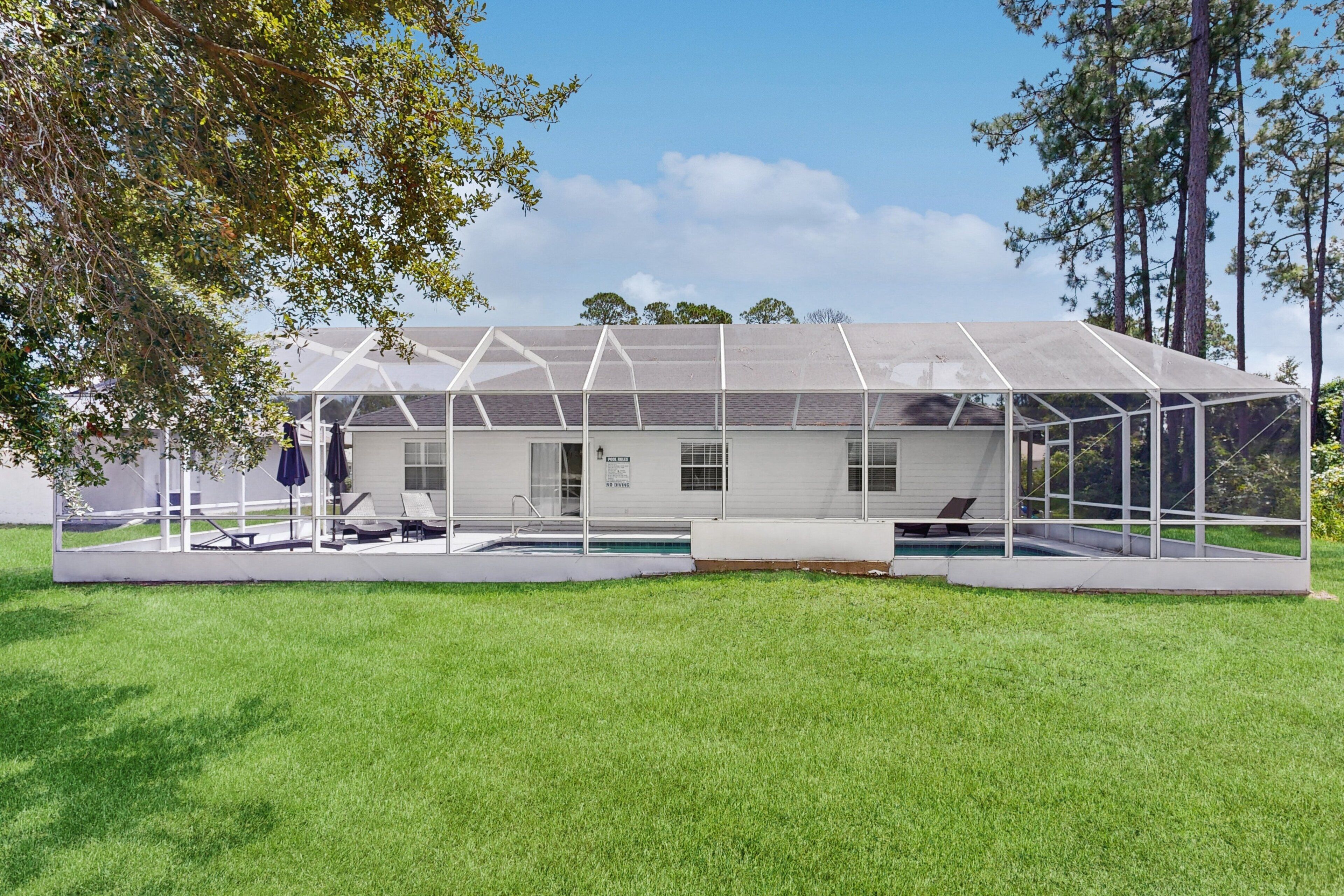 A modern house with a glass enclosure, a swimming pool, and a lawn.
