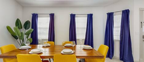 Een eetgedeelte met een houten tafel voor zes personen, gele stoelen en blauwe gordijnen.