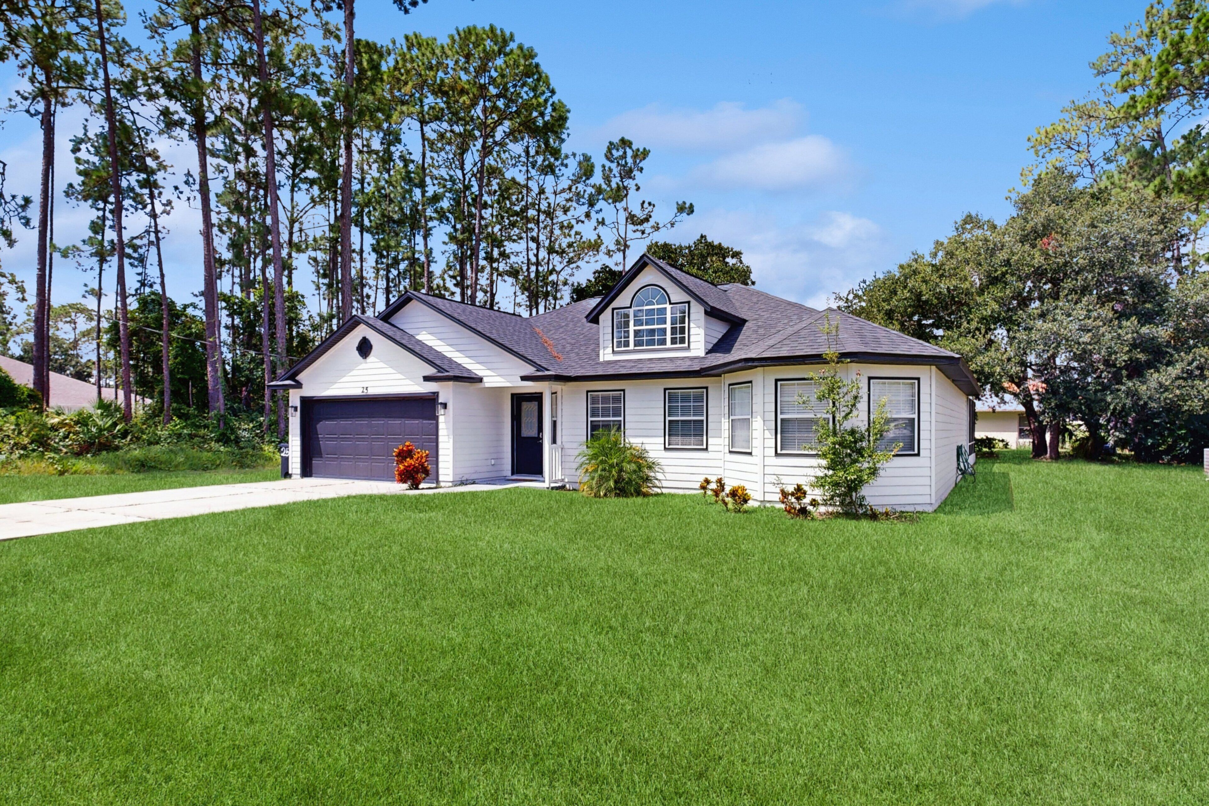 A two-story house with a garage, surrounded by a well-maintained lawn and tall trees.