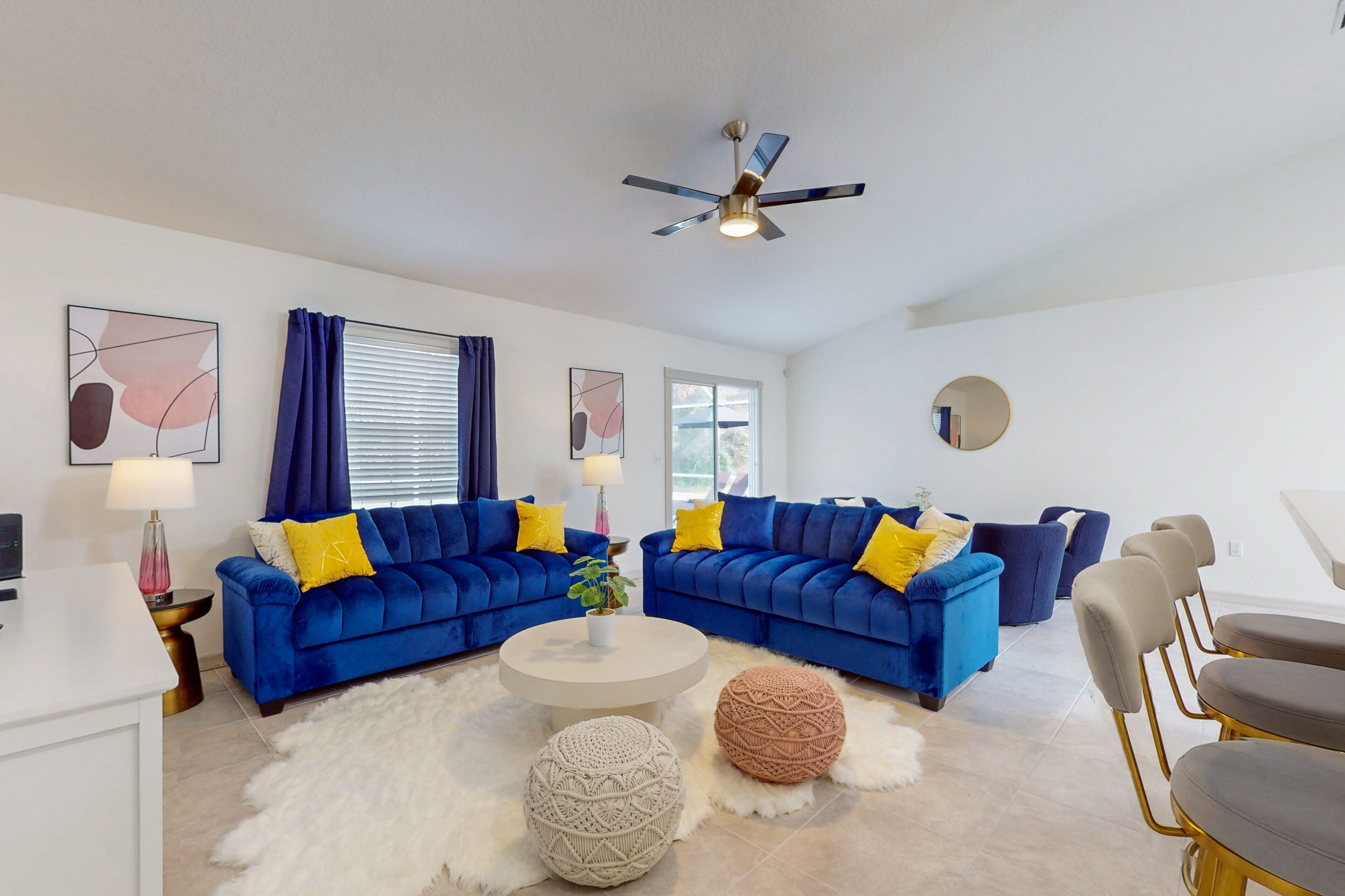 A modern living room with two blue sofas, a white coffee table, and a ceiling fan.