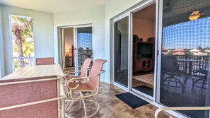 A balcony with a table and chairs, a sliding glass door leading to an outdoor area, and a view of palm trees and buildings. - Luxurious Beach Villa Steps to Cinnamon Beach! Ocean and Lake Views (Palm Coast)