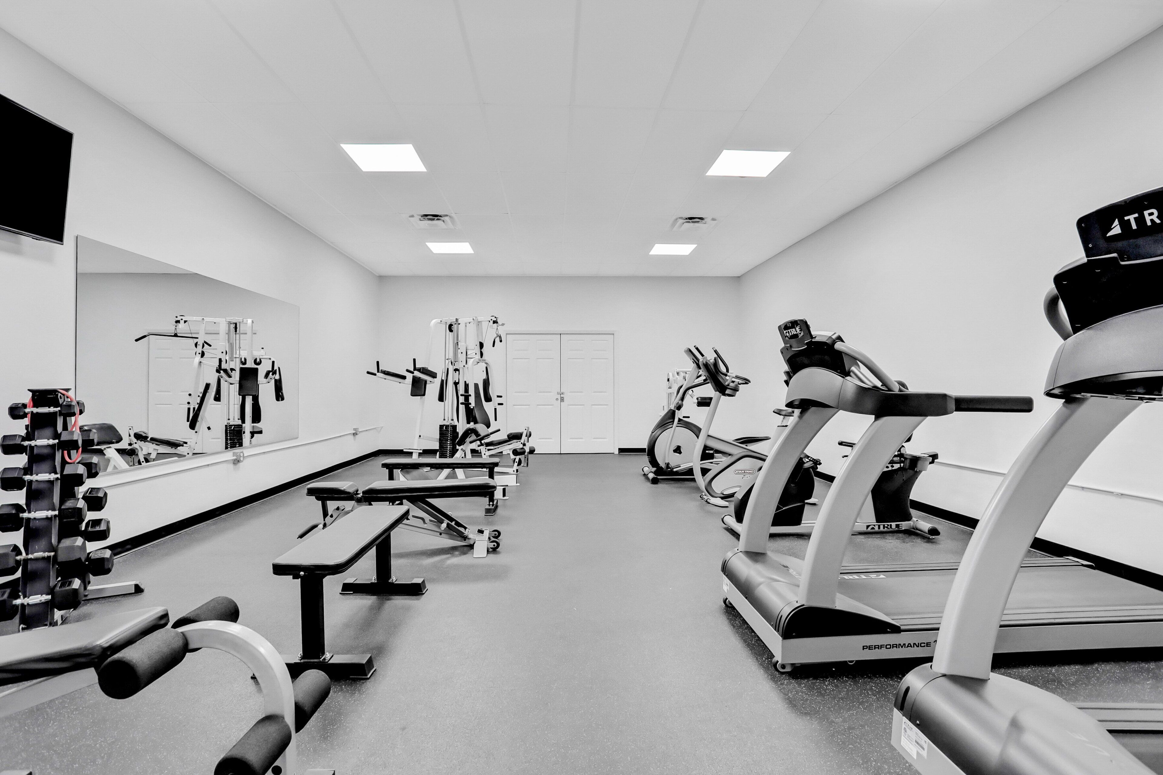 Een sportschool met diverse fitnessapparaten, waaronder loopbanden, krachttoestellen en een bank.