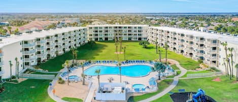 A resort with a central pool, multiple balconies, and a surrounding lawn.