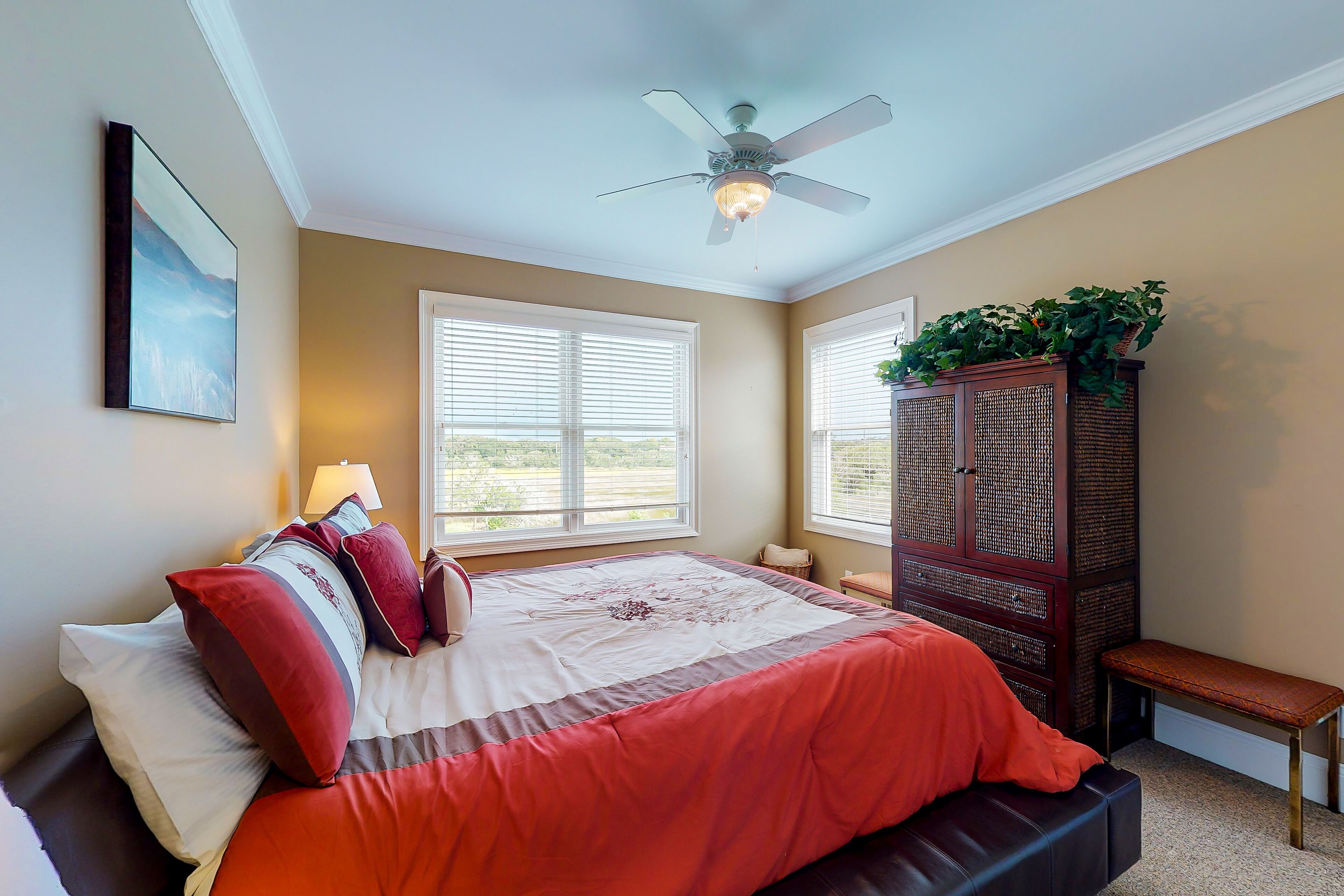 Une chambre à coucher avec un lit, un ventilateur de plafond, une fenêtre, un banc et un meuble avec des plantes.