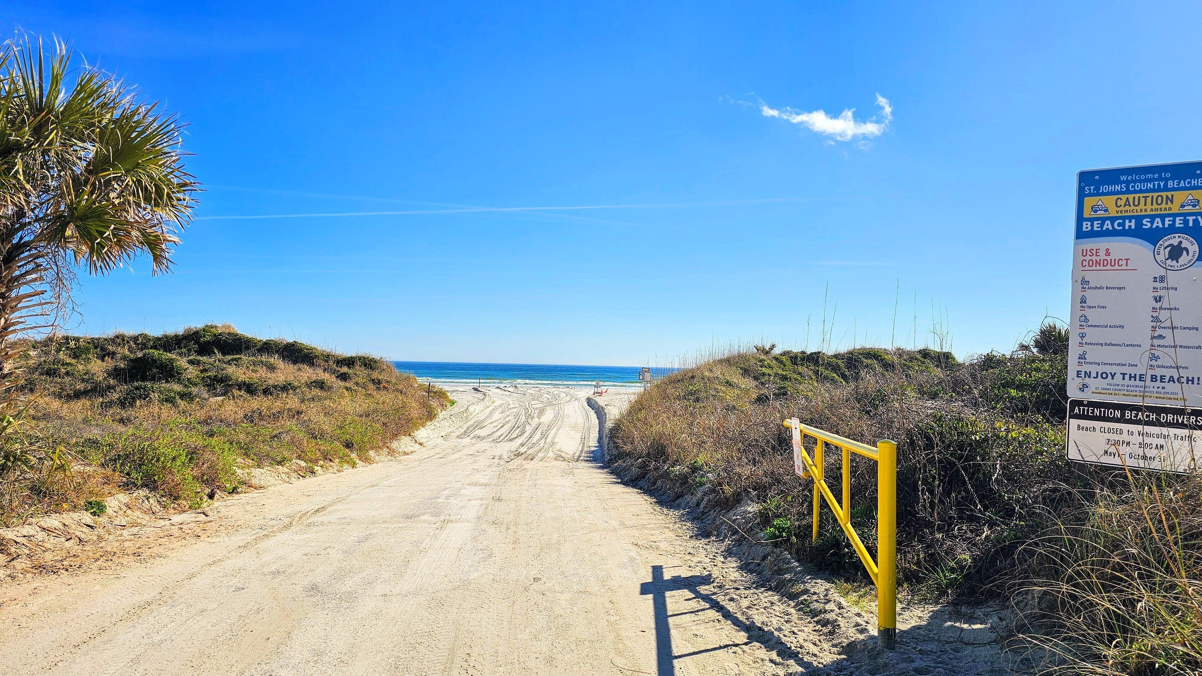 A sandy beach path leading to the ocean with a caution sign and beach safety rules.