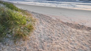 Una spiaggia con un sentiero sabbioso che conduce all'acqua, circondata da erba.