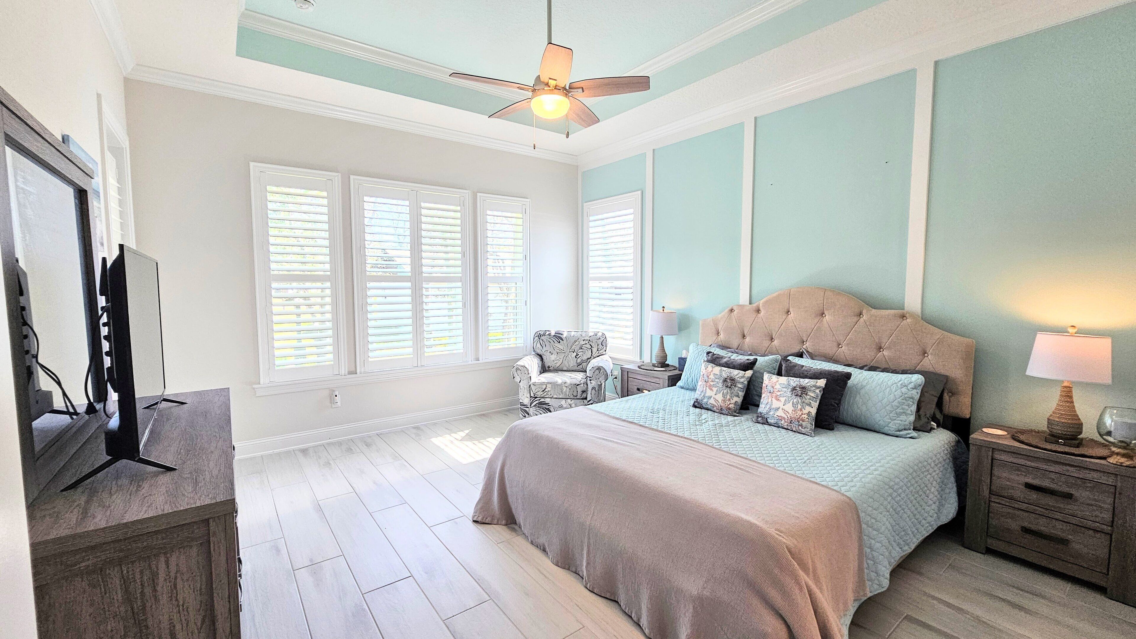 A bedroom with a bed, a chair, a nightstand, a lamp, and a ceiling fan.