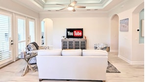 Un soggiorno spazioso con un divano bianco, una ventola a soffitto e un display di YouTube TV.