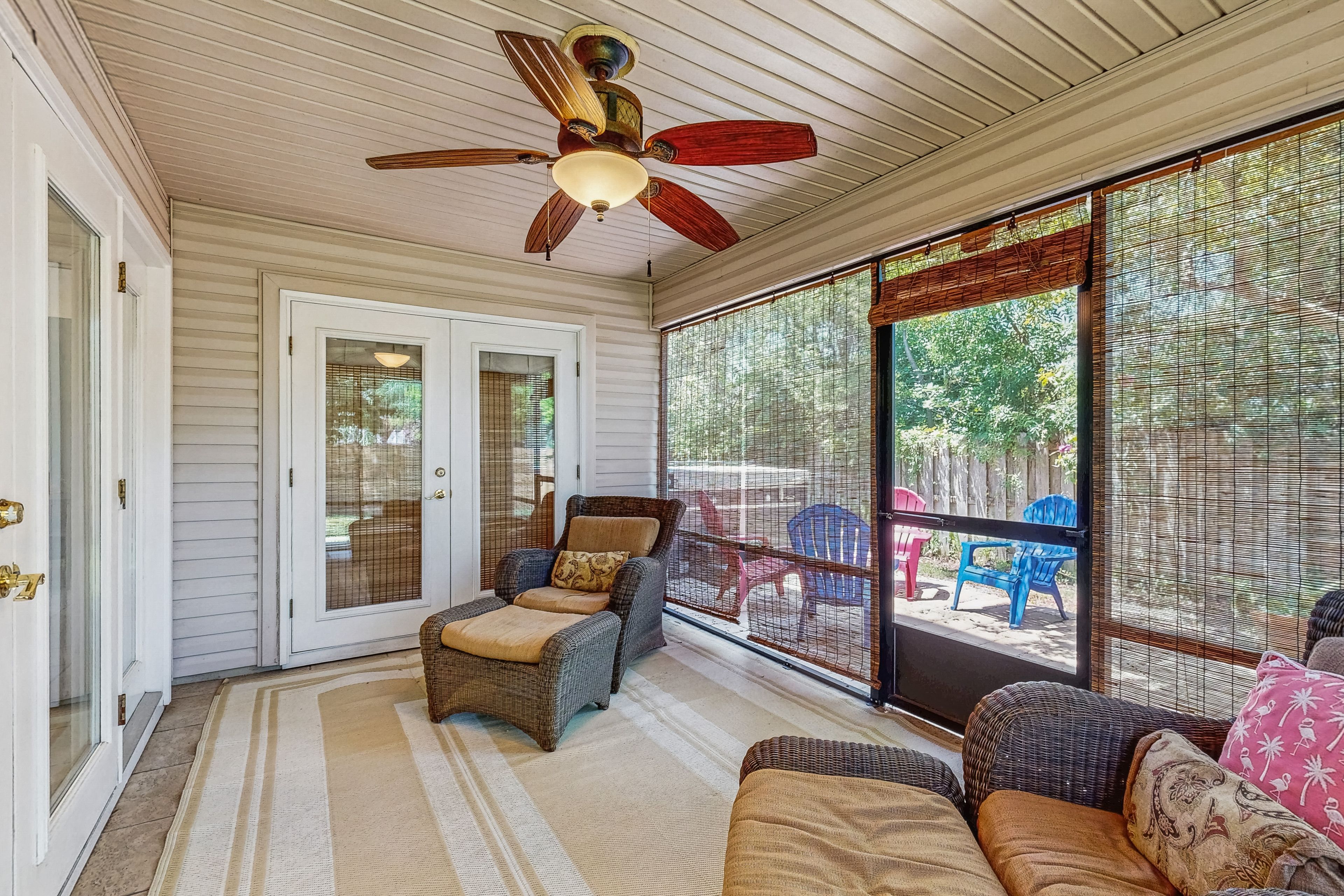 A covered porch with wicker furniture, a ceiling fan, and large windows.