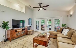 A spacious living room with a large flat-screen TV, a wooden coffee table, a brown leather sofa, and a ceiling fan. - Dog-friendly Home With Enclosed Backyard, Private Hottub and Sunroom (St. Augustine)