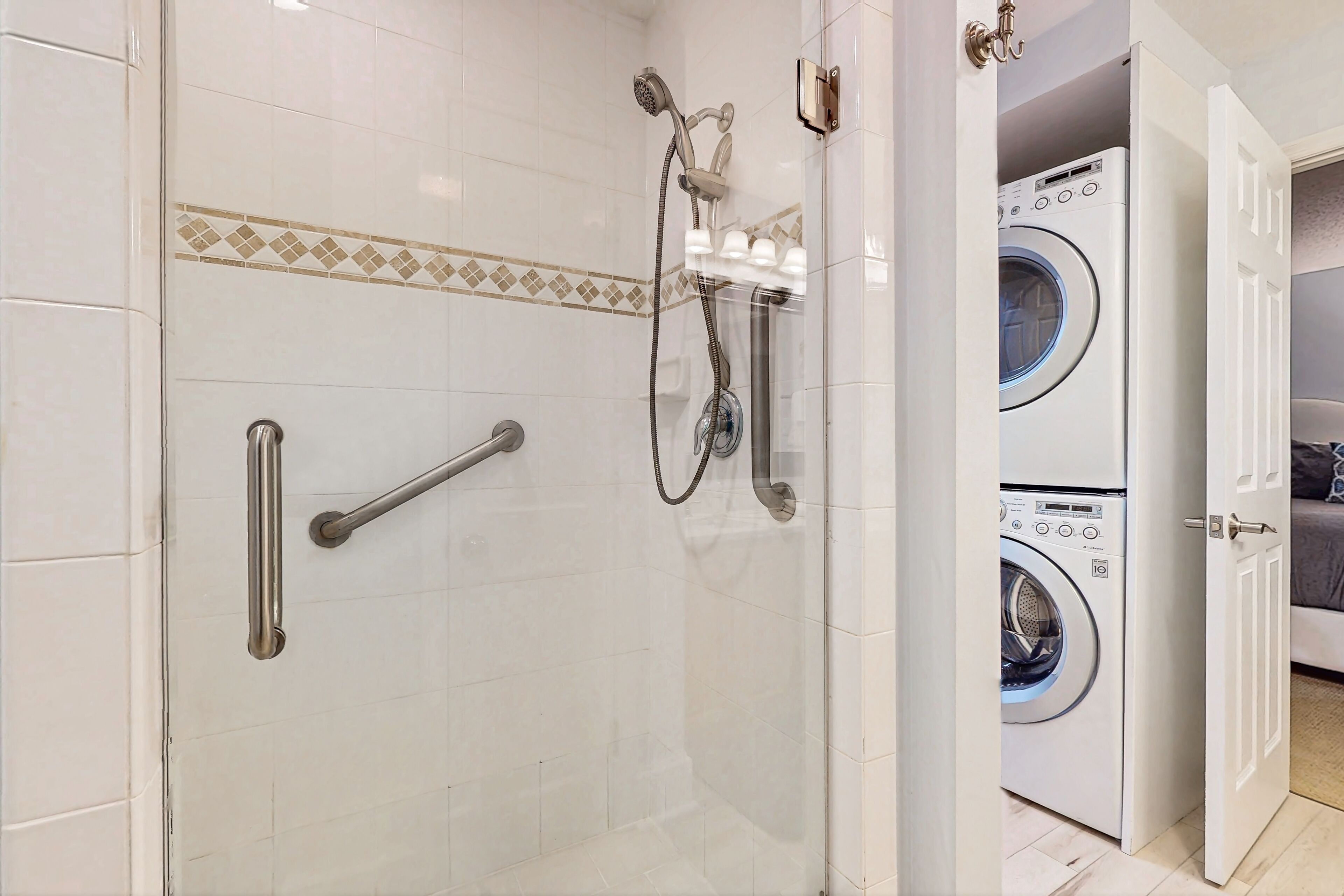 A bathroom with a glass-enclosed shower, a handrail, a towel rack, and a washing machine visible through an open door.