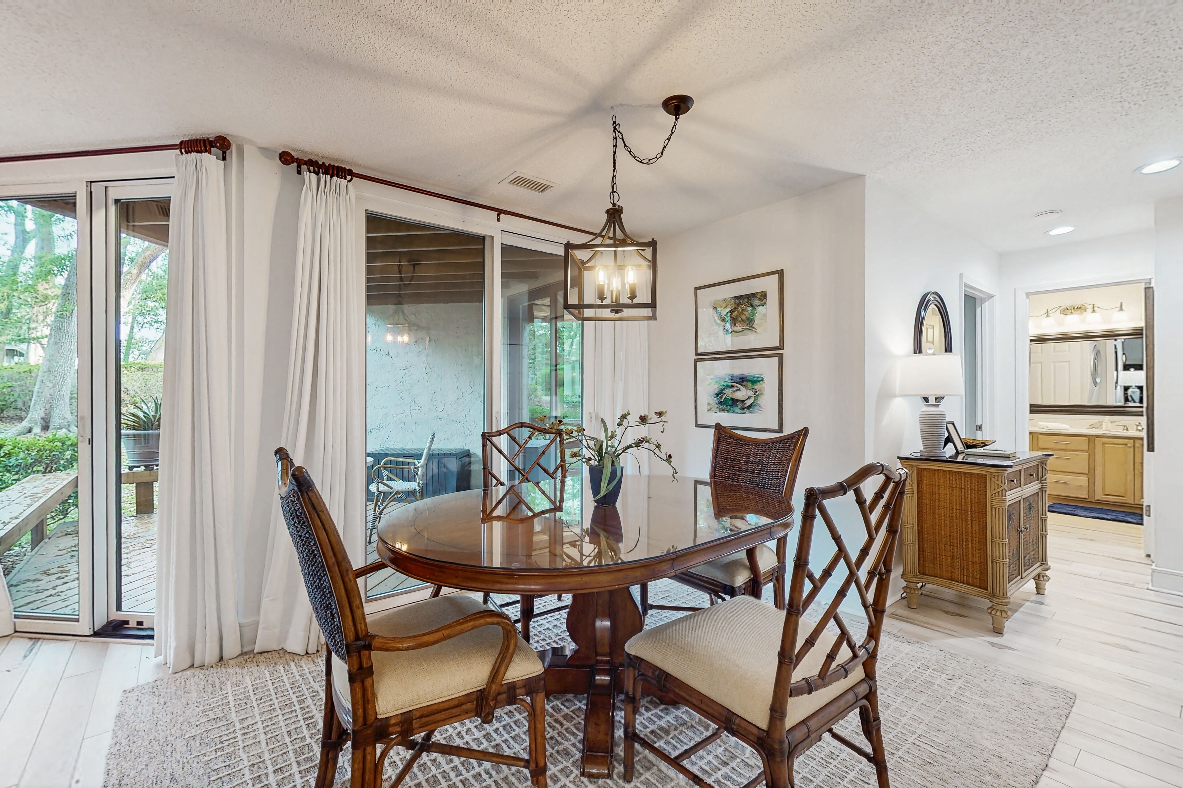 A dining area with a round table, four chairs, a chandelier, and a view of the outdoors through glass doors.