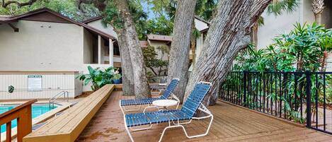 A wooden deck with two blue lounge chairs and a small table, a pool, and a sign reading "POOL RULES".
