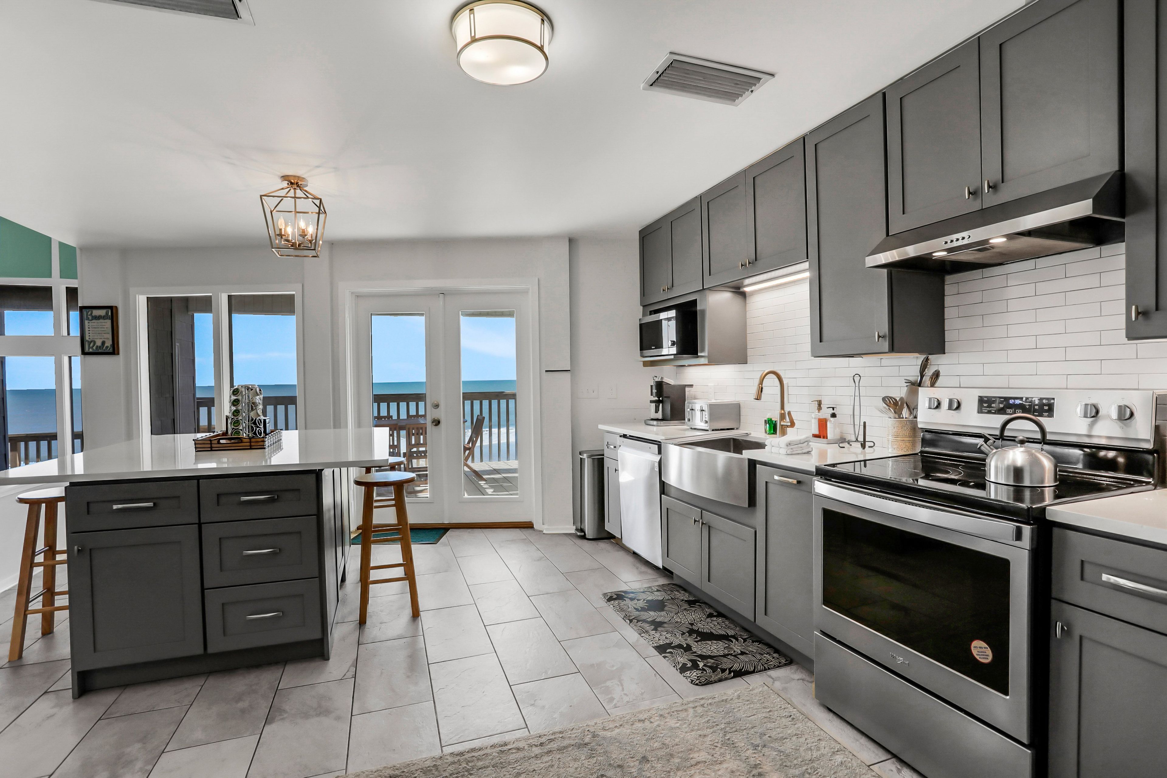 A modern kitchen with grey cabinets, stainless steel appliances, and a large island.