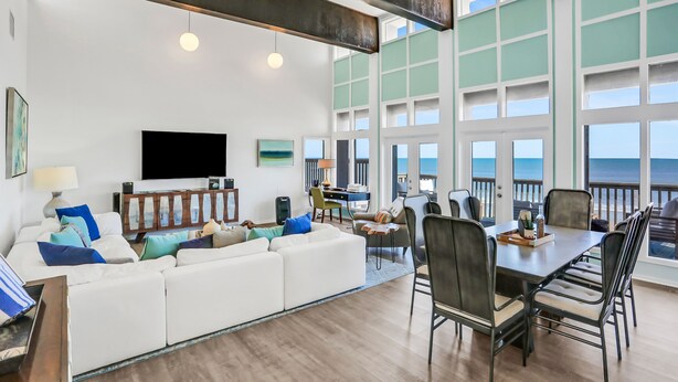 A modern living room with a white sofa, a dining table with chairs, and a large TV on the wall. - Gorgeous Beachfront Home With Inviting Deck & Patio, Hammock, Amazing Views (St. Augustine)