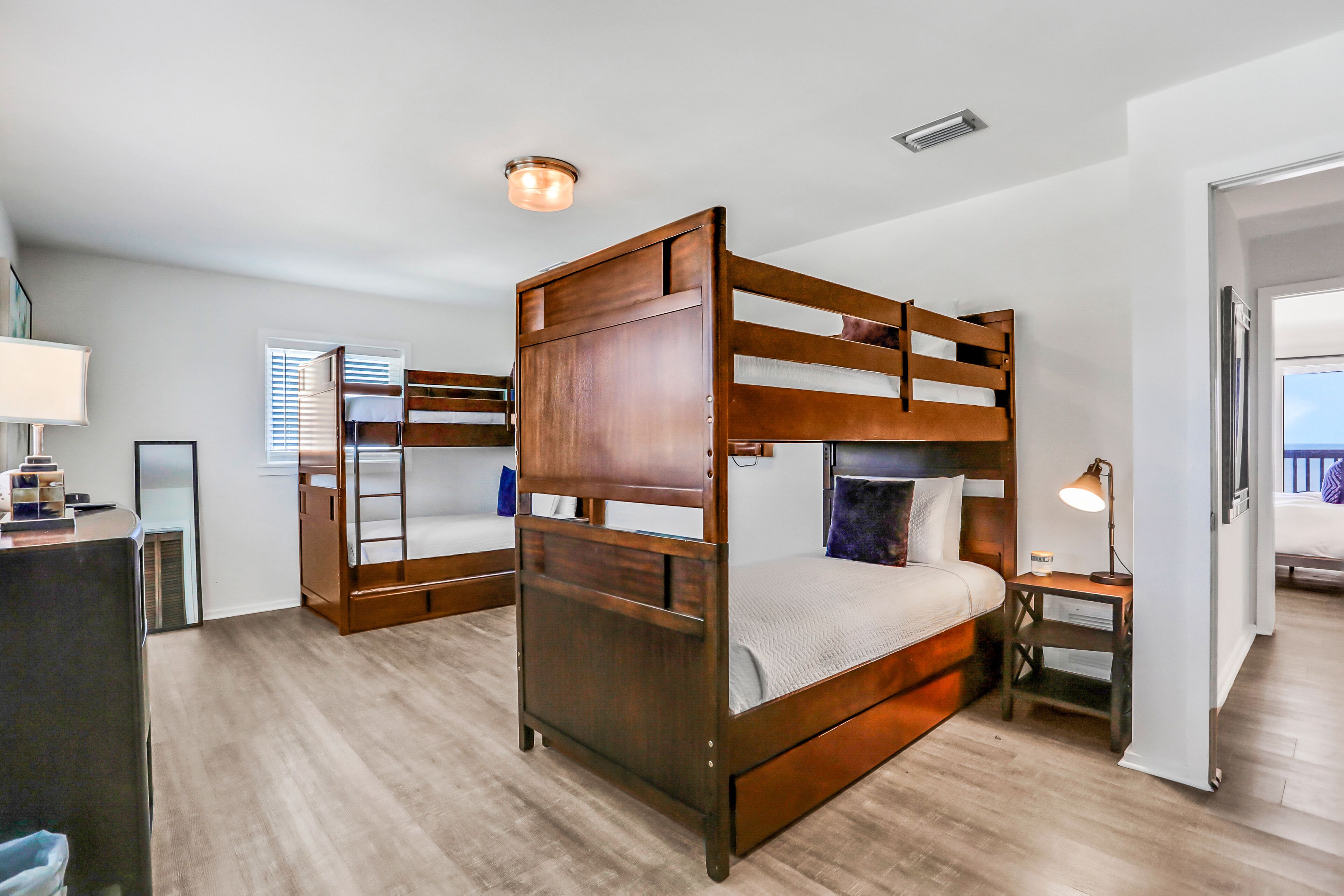 A room with a bunk bed, a desk, a lamp, and a window with blinds.