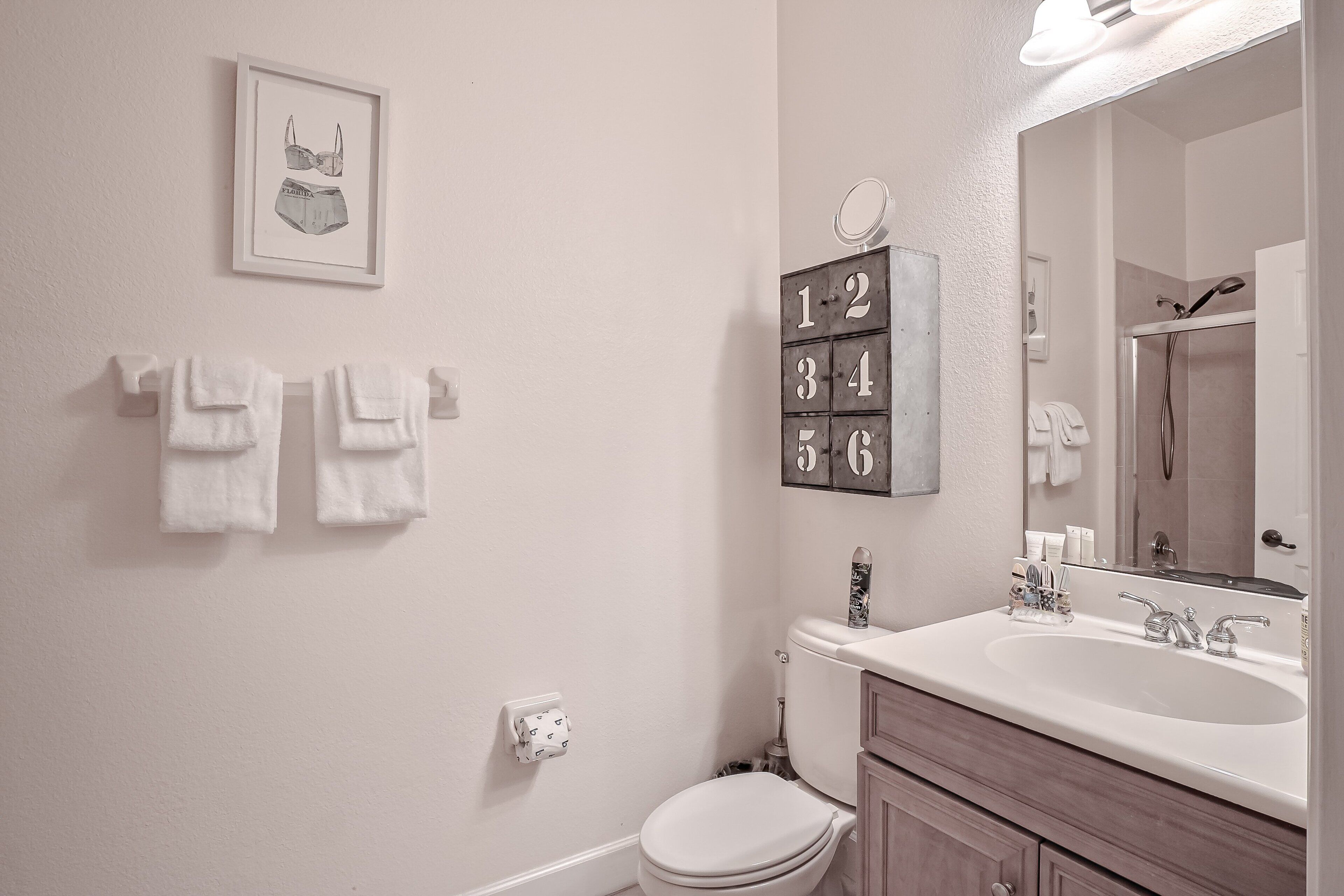 A bathroom with a white sink, a toilet, a mirror, and a framed picture on the wall.