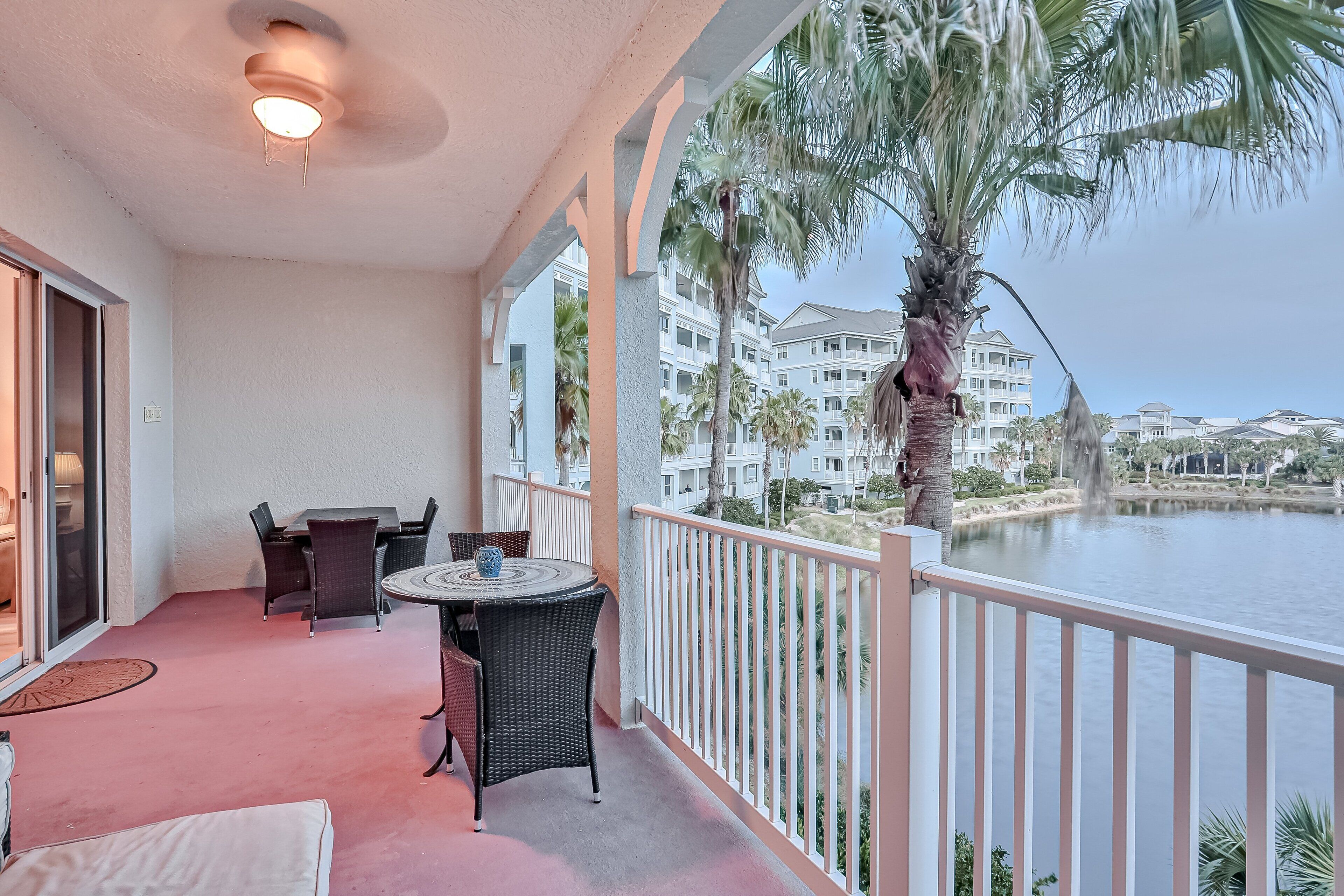 A balcony with a table and chairs, overlooking a body of water and palm trees.