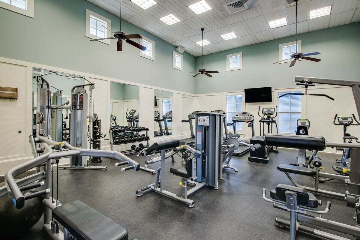 A gym with various exercise equipment, mirrors, and ceiling fans.