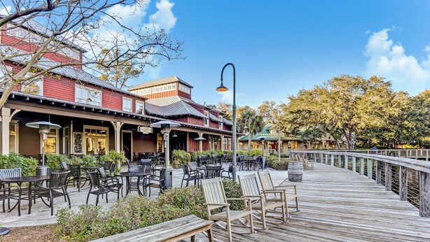 A wooden deck with outdoor seating and a building with a red facade in the background. - Dog-friendly Home in the Tennis Villas W/free Wifi, Shared Pool, Central AC (Fernandina Beach)