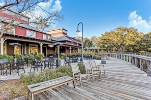 A wooden deck with outdoor seating and a building with a red facade in the background. - Dog-friendly Home in the Tennis Villas W/free Wifi, Shared Pool, Central AC (Fernandina Beach)