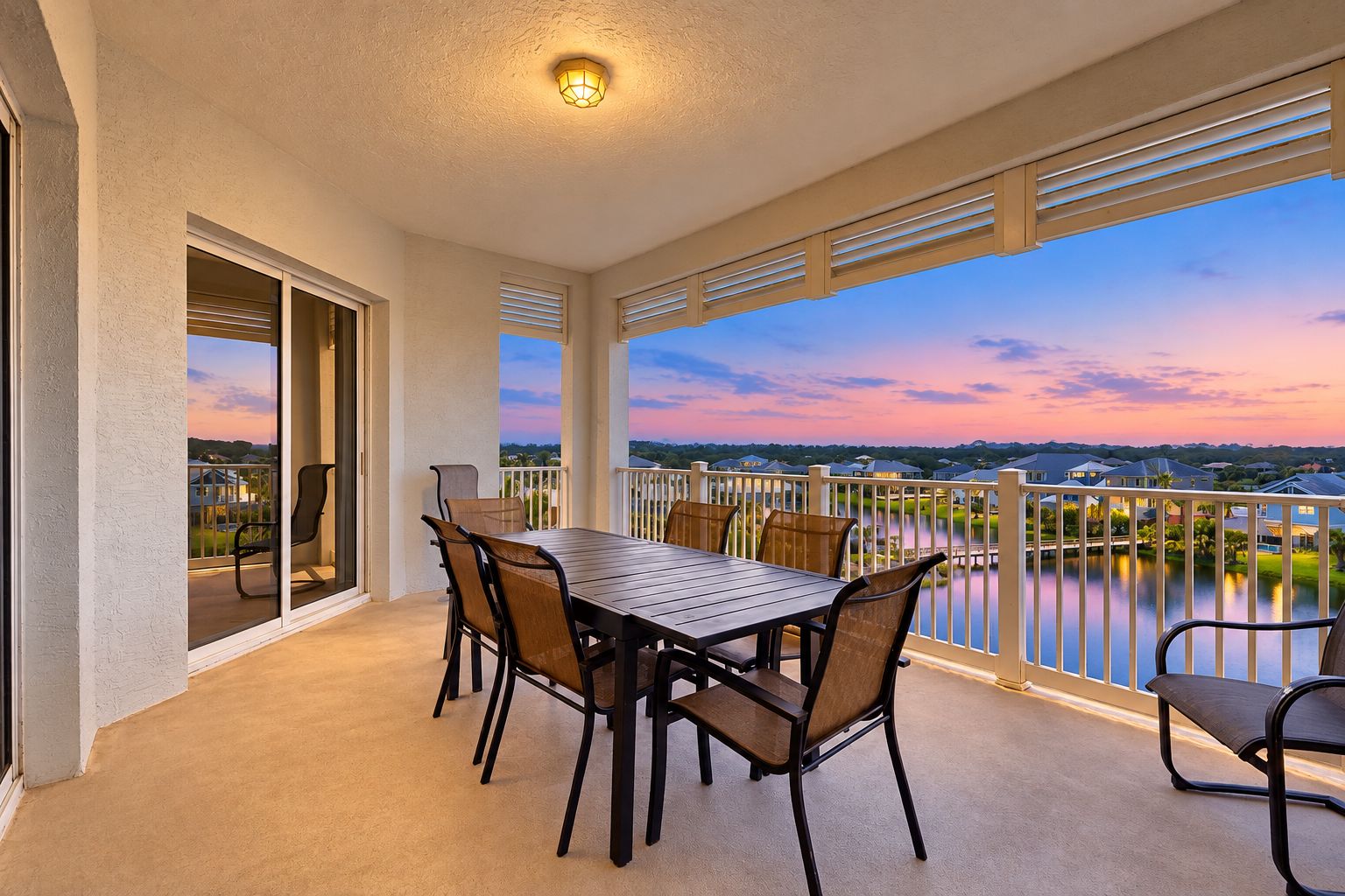 A balcony with a table and chairs, a view of a lake, and a sunset.