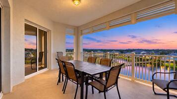 A balcony with a table and chairs, a view of a lake, and a sunset.