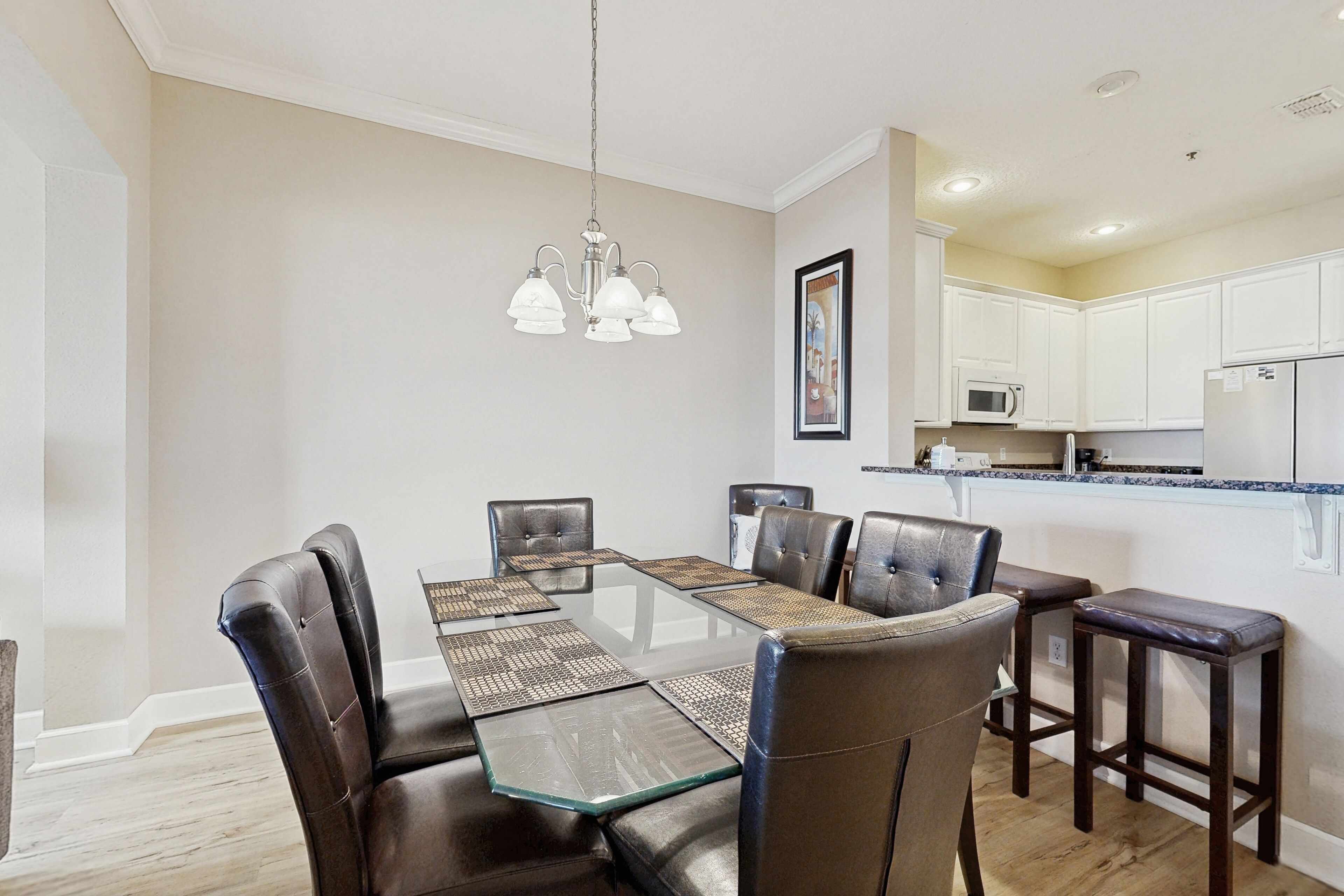 A dining area with a glass-top table, leather chairs, and a chandelier.