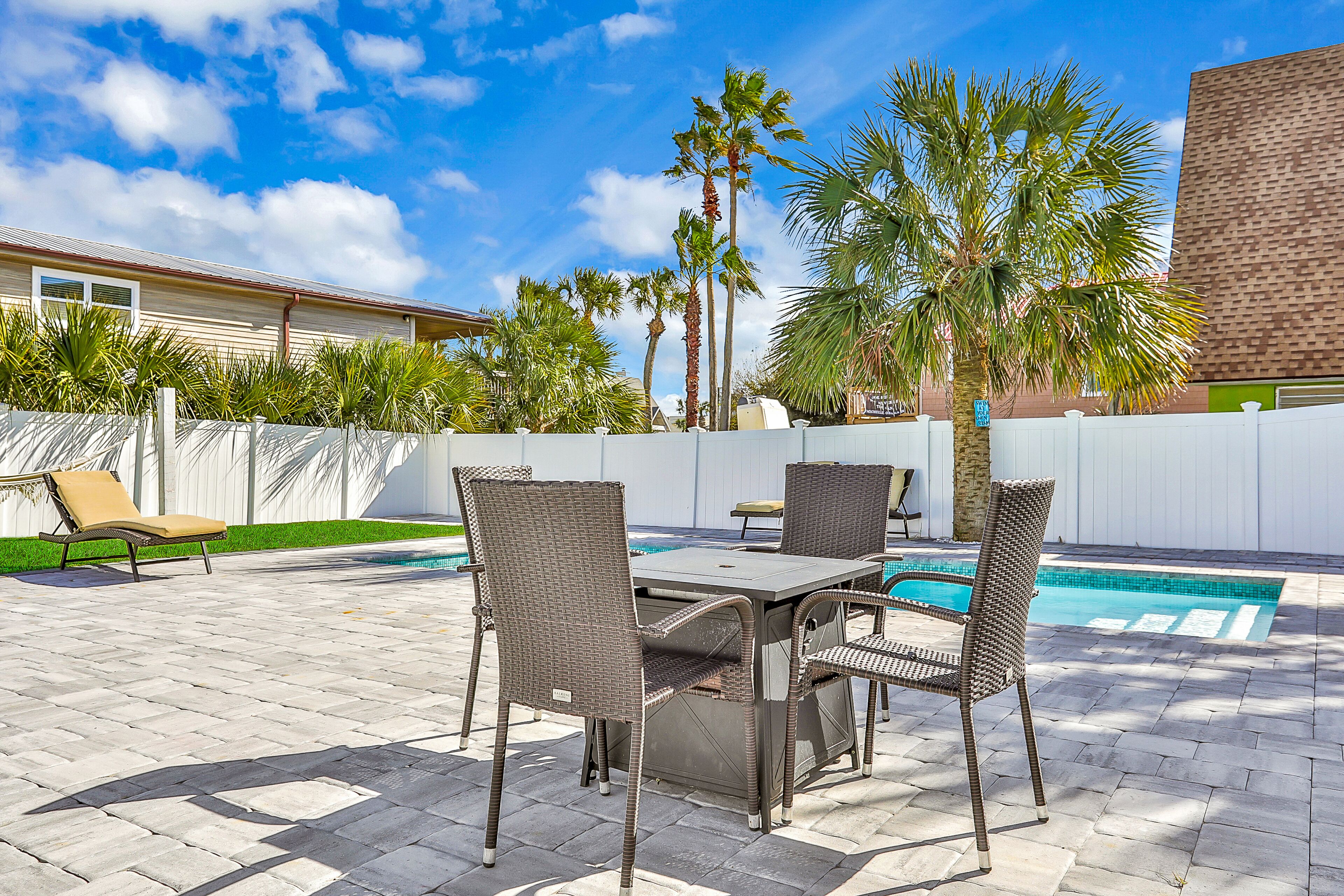 An outdoor patio with a pool, surrounded by palm trees and a white fence.