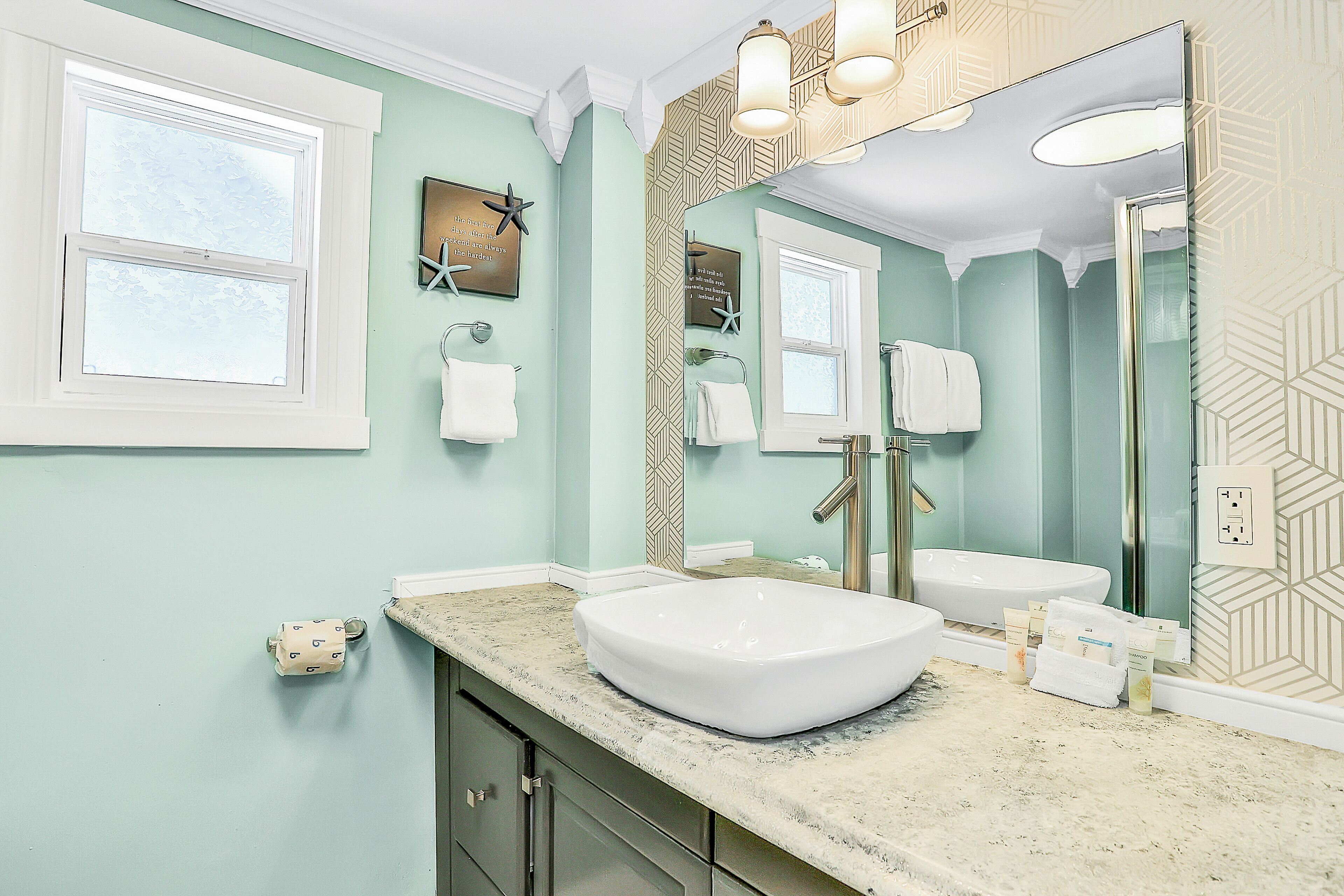 Un baño con un espejo grande, un lavamanos blanco y un mueble de tocador con encimera.