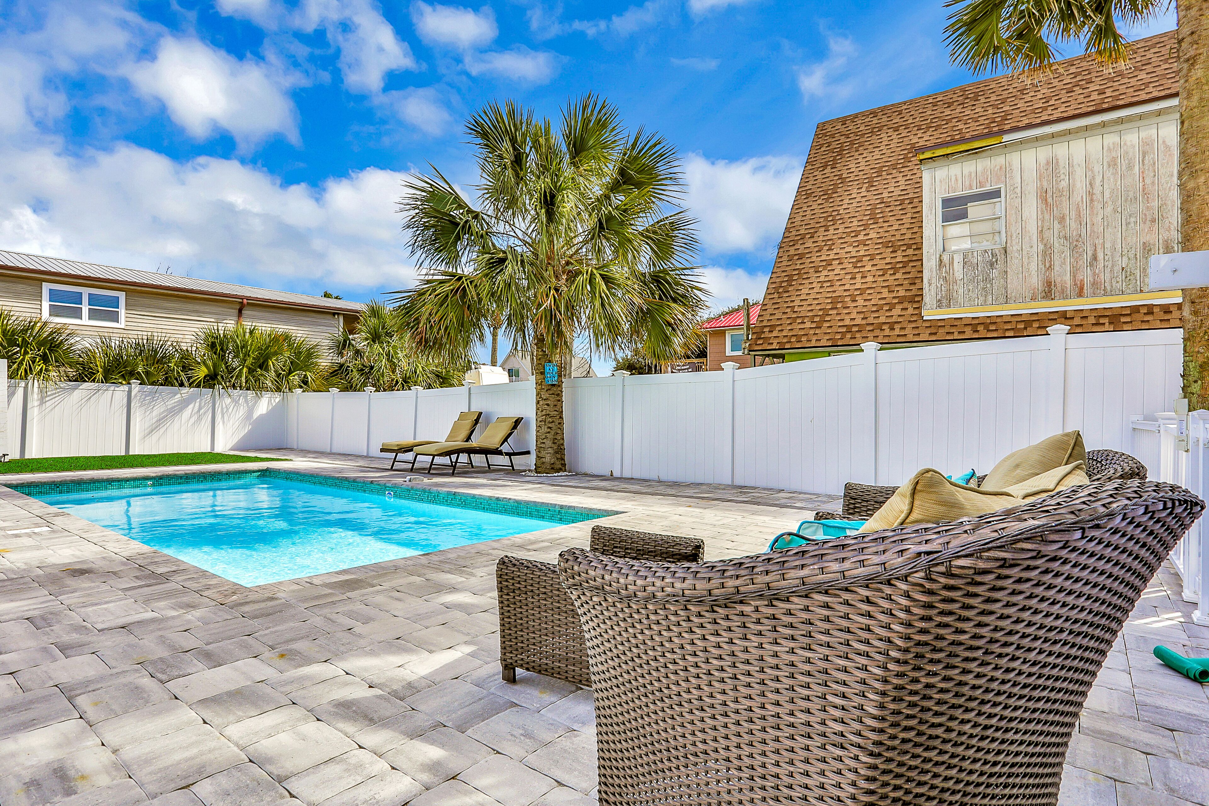 A backyard with a swimming pool, wicker furniture, and a palm tree.