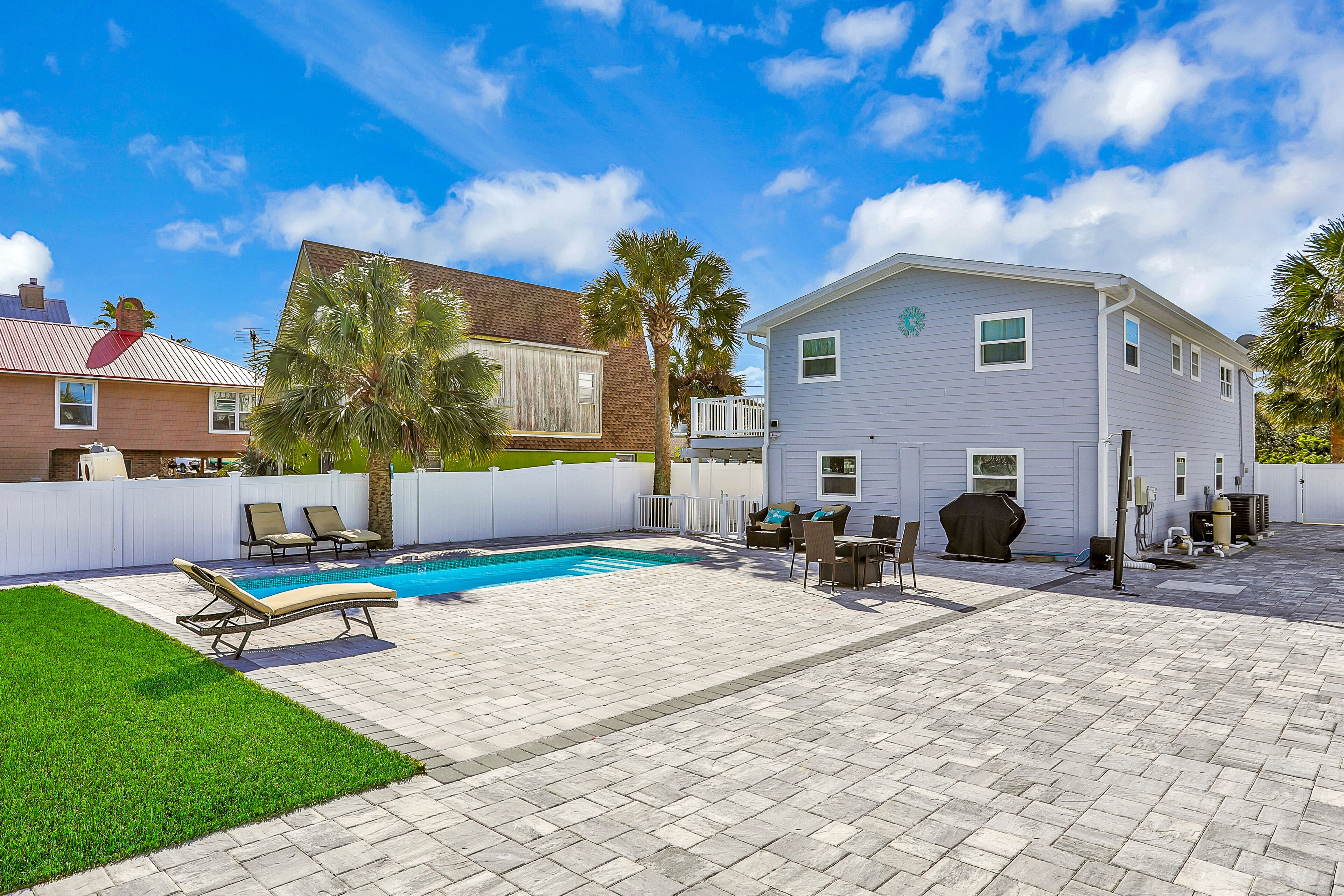 A backyard with a swimming pool, patio furniture, and a white fence.