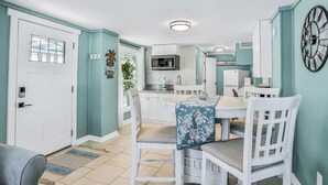 Un comedor con una mesa dispuesta para dos personas, sillas blancas y mantel azul.