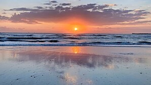 Una playa con el sol poniéndose sobre el océano, creando una superficie de agua tranquila y serena.