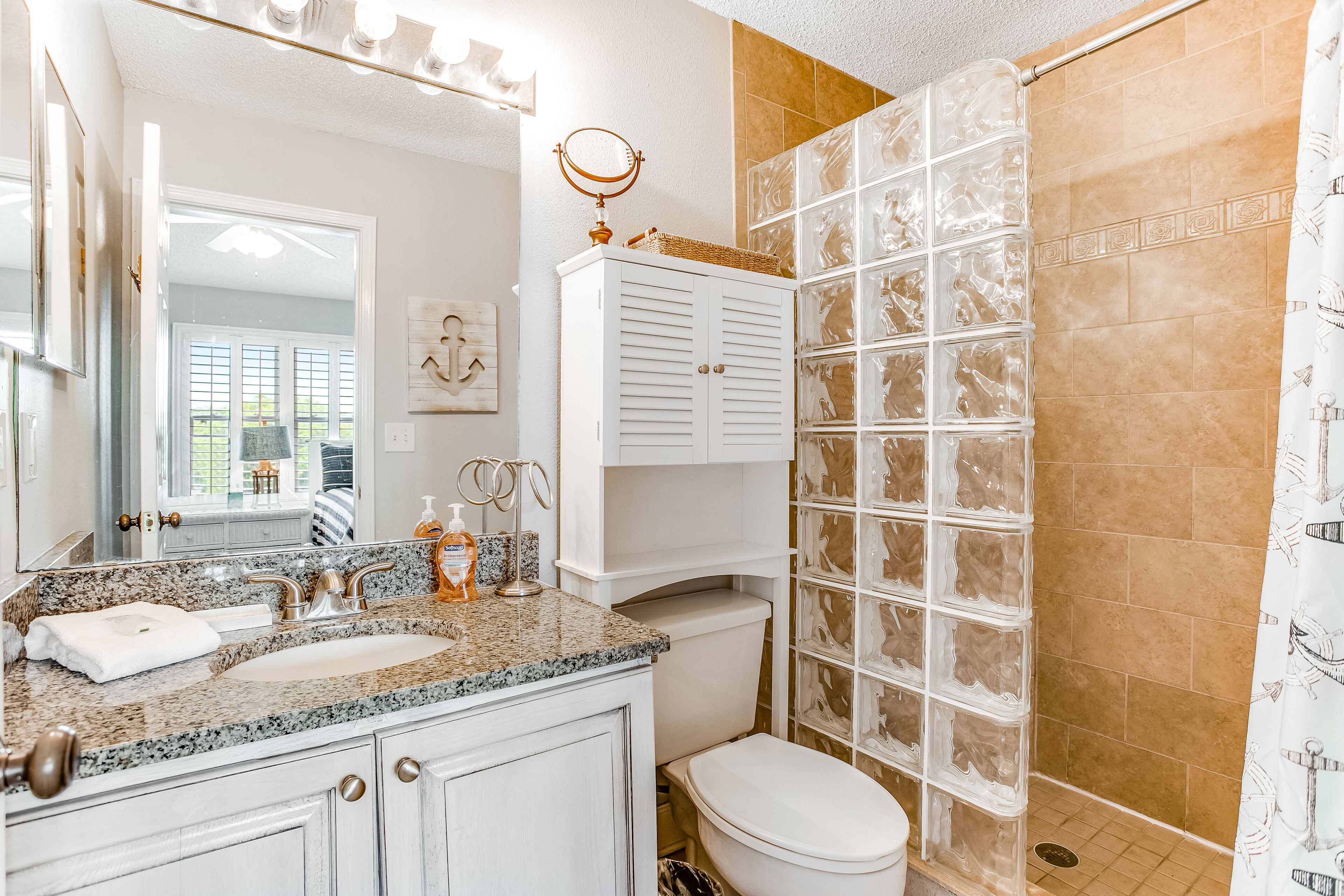 A bathroom with a granite countertop, a white toilet, a vanity with a mirror, and a shower with patterned tiles.