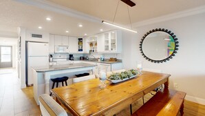 A modern kitchen with white cabinets, a wooden dining table, and a large mirror on the wall. - First Floor Oceanfront Condo With Beach Access and Tennis Courts (St. Augustine)