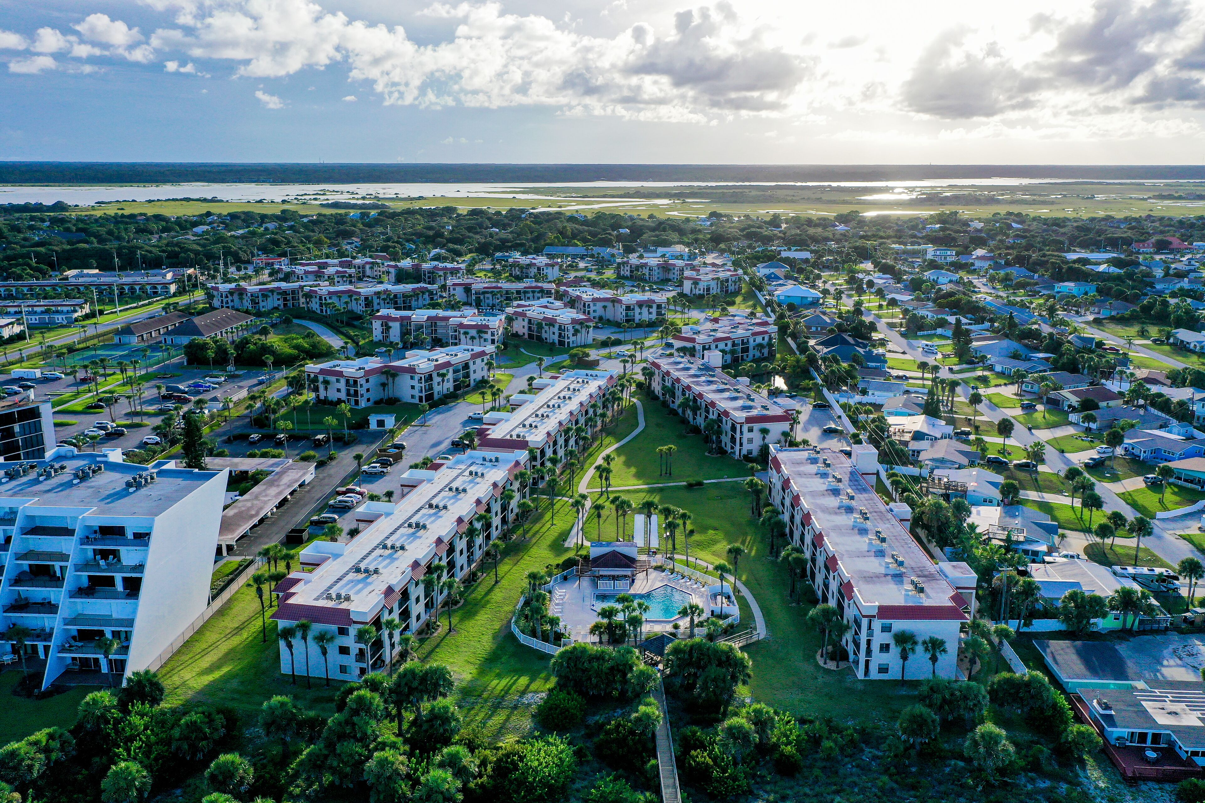 An aerial view of a resort with multiple buildings, a central pool area, and surrounding greenery.