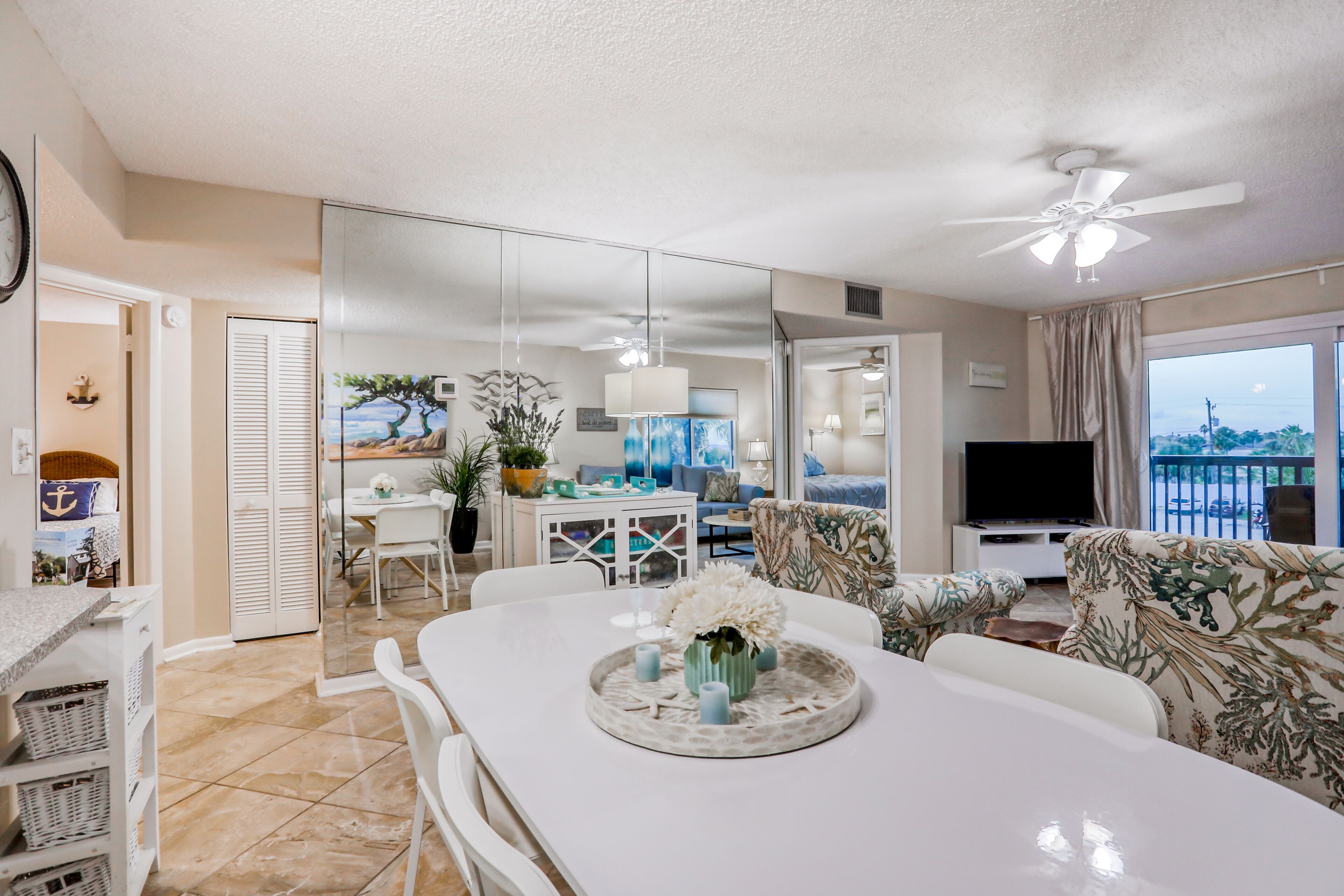 A spacious living area with a dining table, chairs, a sofa, and a TV. There is a balcony with a view.