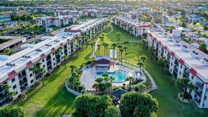 Ett hotellkomplex med flera byggnader, ett centralt poolområde och omgivande grönska.