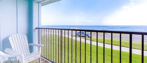 A balcony with a white chair, a view of the ocean, and a road with vehicles.