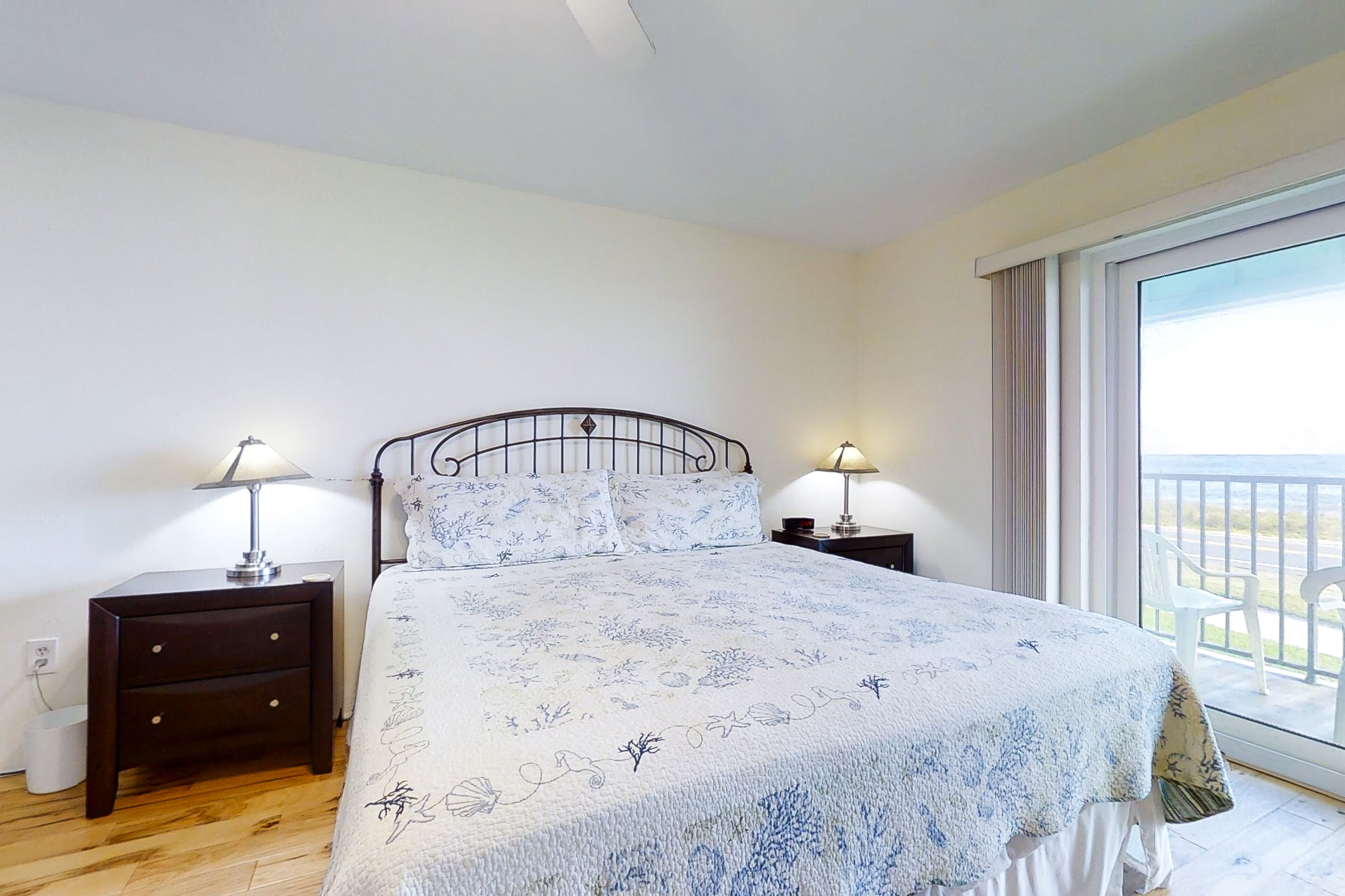 A bedroom with a bed, two bedside tables with lamps, a window with a view, and a wooden floor.
