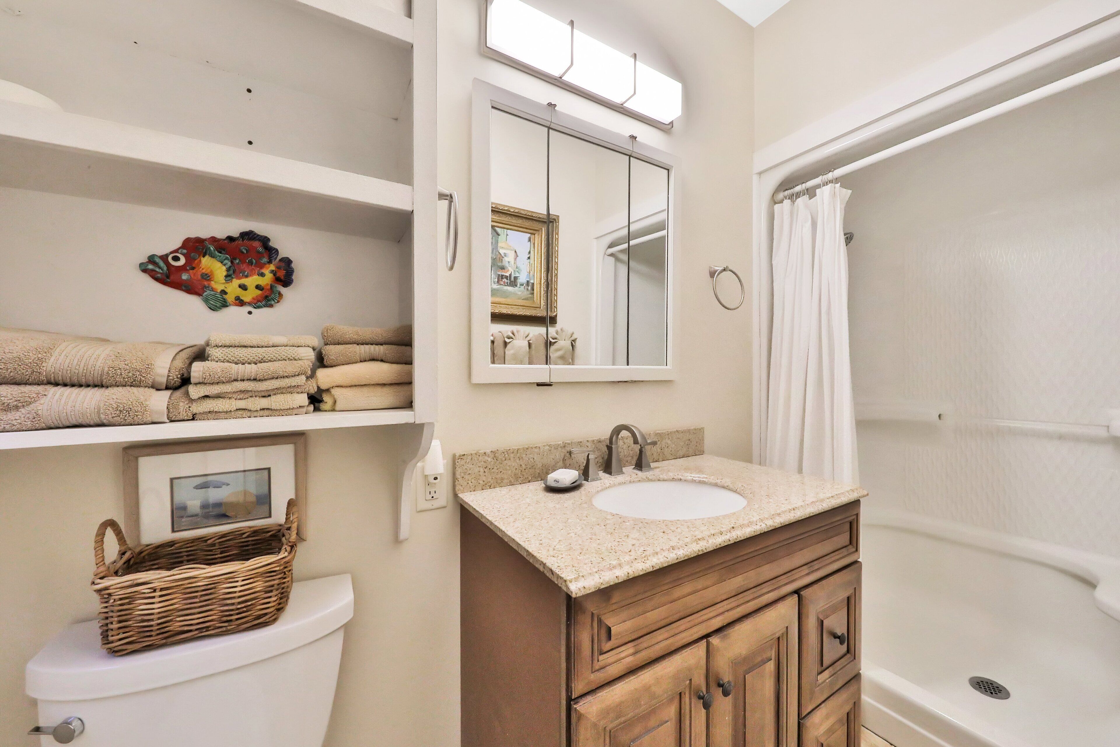 A bathroom with a toilet, a sink with a mirror above it, a bathtub, and a shelf with towels and a basket.
