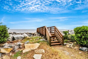 Eine Holztreppe führt zu einem Strand unter blauem Himmel.