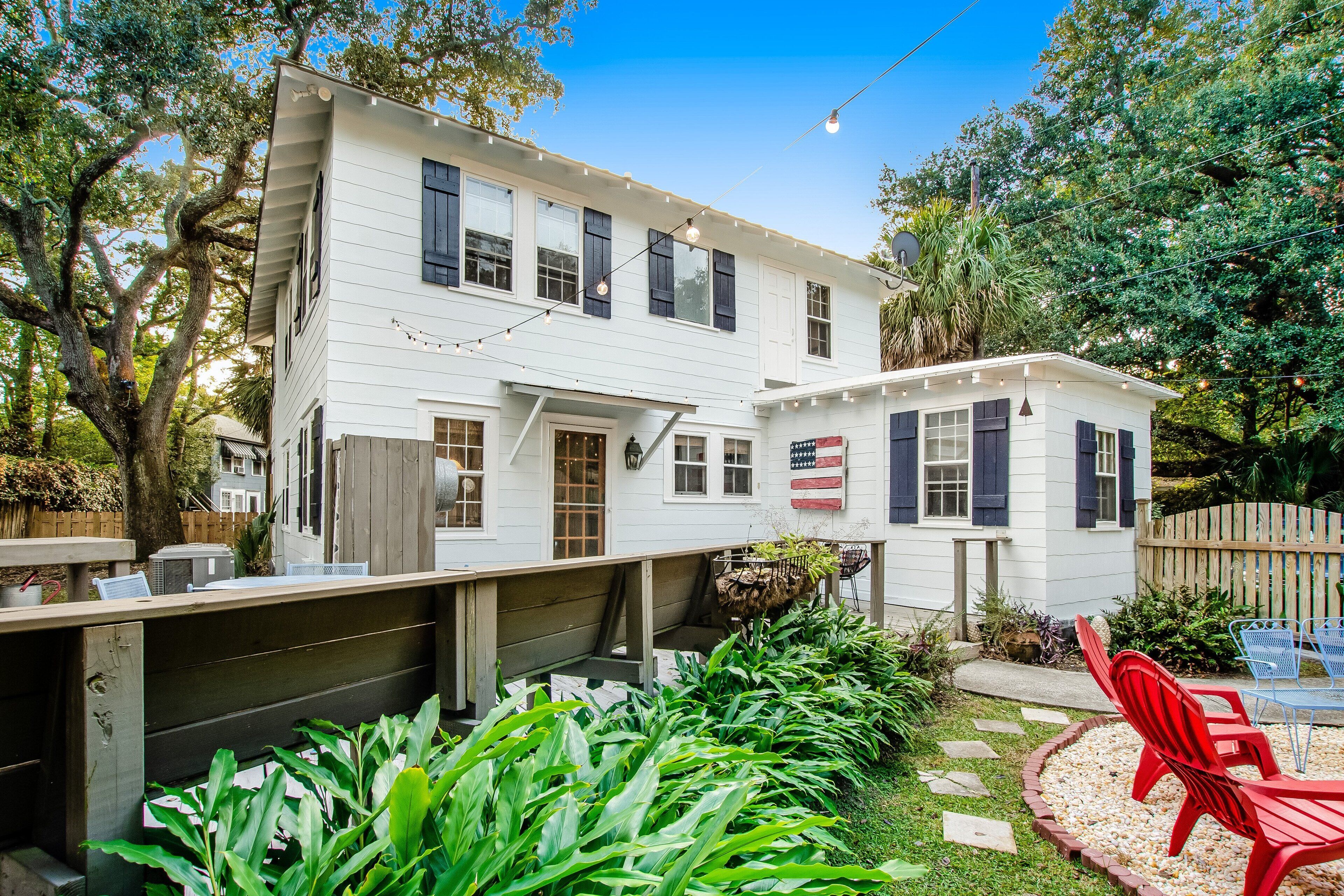A white house with a porch, a red chair, and a garden with plants.