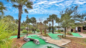 Een minigolfbaan met groene putting greens, een vijver en palmbomen.