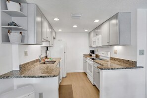 Una cocina moderna con gabinetes blancos, encimeras de granito y electrodomésticos integrados.