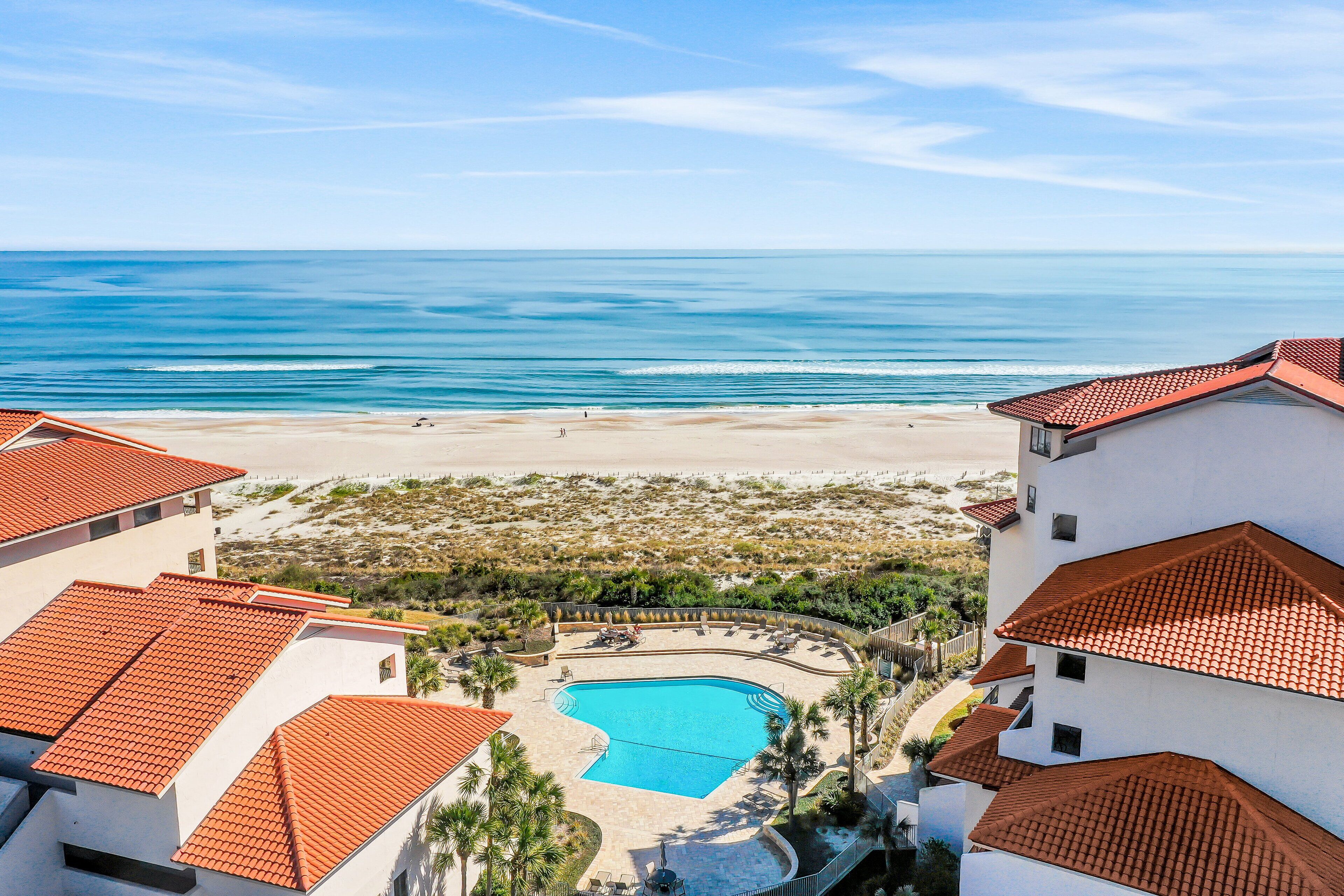 Ein Resort mit Swimmingpool, umgeben von Gebäuden mit roten Ziegeldächern, mit Blick auf einen Strand und den Ozean.