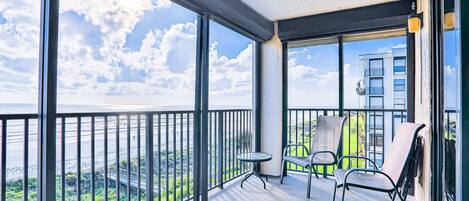 A balcony with a glass railing, a small round table, and two chairs.